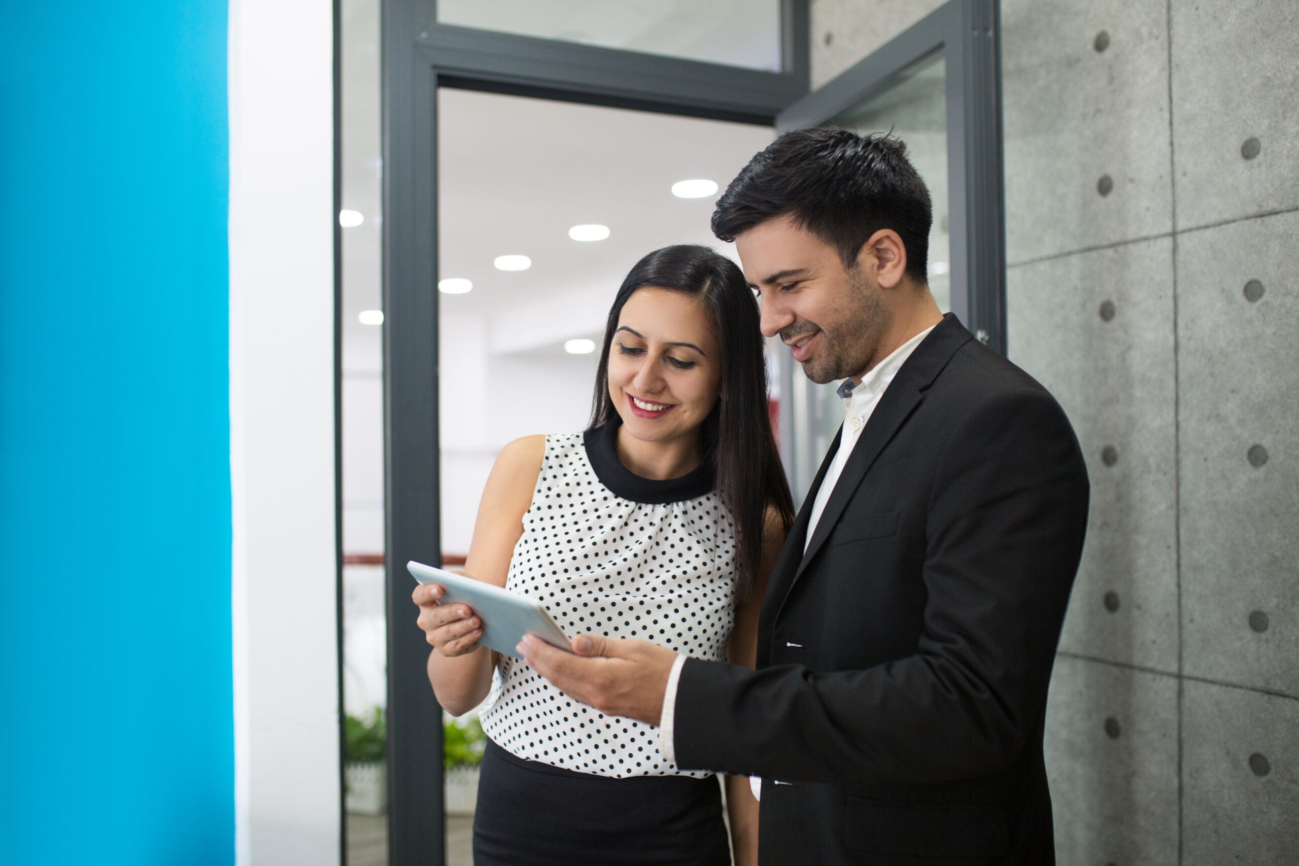 Portrait of cheerful young colleagues browsing on digital tablet. Young Caucasian businesswoman and businessman standing together in doorway using pc tablet. Technology in business